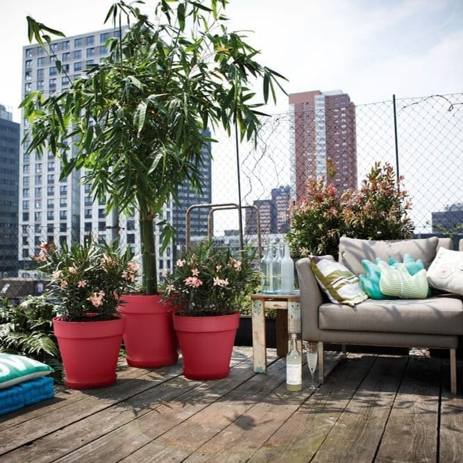 Macetas rojas grandes con plantas en una terraza de suelo de madera