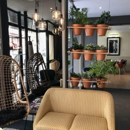 Macetas de barro con plantas en estantes junto a una butaca de un interior luminoso